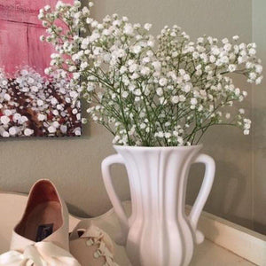 White vase with handles displayed with flowers, fancy lady’s shoes
