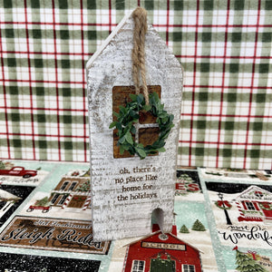 Wooden block holiday house with a seasonal message and small hanging wreath