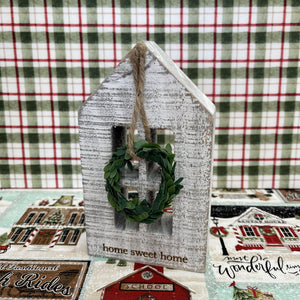 Wooden block holiday house with a seasonal message and small hanging wreath