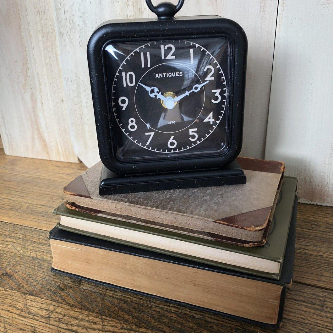 Small metal bookcase clock with white lettering and small round handle on top